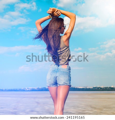 Beautiful slim tanned fitness   girl \'s back  with  hands on top. Posing outdoor in stylish jeans shorts. Soft light.