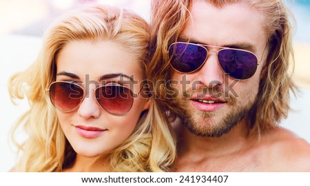 Young beautiful stylish couple in love posing on the sunny beach , wearing sunglasses,  handsome guy and cute blonde with curl  hairstyle  . Bright sunny colors.