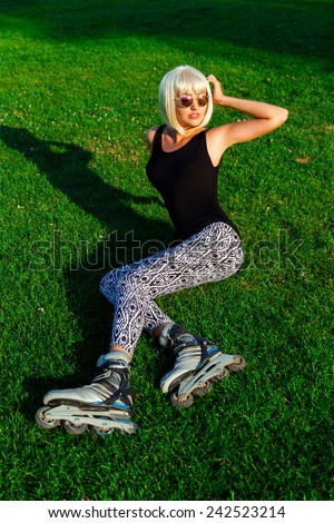 Pretty young girl  in with wig  and sunglasses wearing roller skates sitting on grass in the park and enjoying spring ,