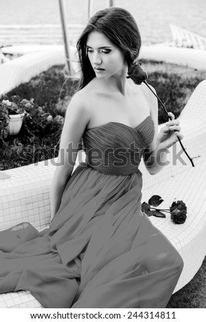 Stylish elegant  gorgeous  woman in long cocktail  dress sitting near luxury swimming pool . Black and white colors.