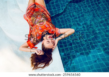 Beautiful sexy woman relaxed near pool after spa, having fun at her vacation in luxury resort, wearing stylish elegant  bright beach dress.