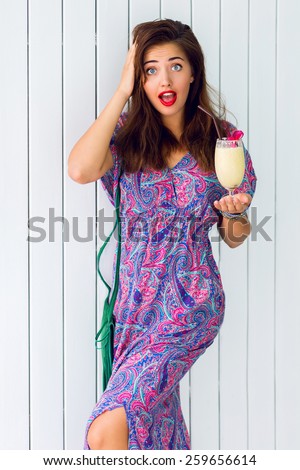 Beautiful woman with surprise face   holding cocktail wearing long psy boho dress and leather bag .