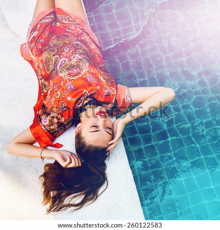 Beautiful sexy woman relaxed near pool after spa, having fun at her vacation in luxury resort, wearing stylish elegant bright beach dress. Instagram colors.