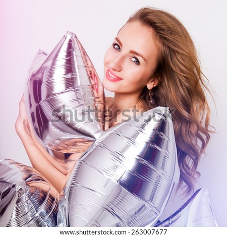 Close up fashion portrait of beautiful elegant young woman  hugging silver party balloons . Pretty lady smile and looking at camera. Bright Instagram colors, party mood. White background.