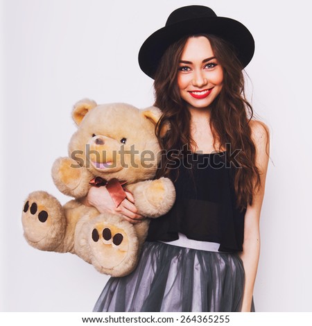 Close up  portrait of pretty cute young woman in stylish hipster outfit  with big eyes , red lips and perfect skin  holding her fluffy teddy bear against white urban wall.
