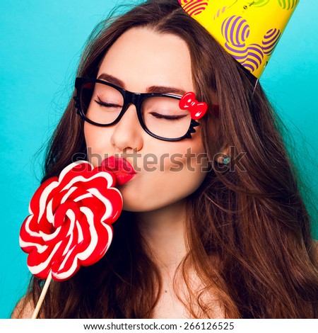 Studio closeup colorful portrait of young sexy funny fashion crazy  woman kiss big lollipop wearing summer  clothes ,  paper hat and cute glasses.