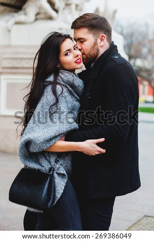 Fashion outdoor  romantic  portrait of beautiful  young couple in love  kissing and hugs  on the street. Wearing  stylish fall outfit ,black leather bag and coat.