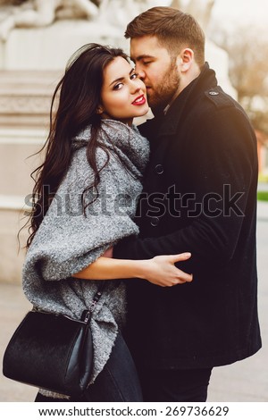 Outdoor fall portrait of fashionable pretty young couple wearing  trendy   monochrome outfit . Two lovers posing against  theater background in  autumn  sunlight.