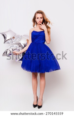 Beautiful young blonde woman celebrate prom and holding  silver party balloons. Wearing blue evening elegant dress and have day of.