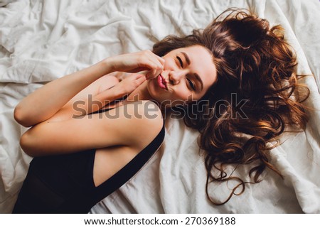Pretty happy young lady  in elegant black lingerie with perfect slim body   lies on  her white bed , flirting and grimaces.