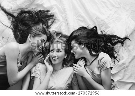 Top view of three best friends tell secrets in  bed . Group of pretty  young  women  in pajamas  lie on back and have fun. Black and white.