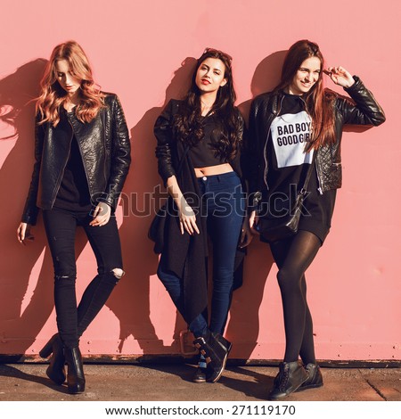 Fashion lifestyle  photo of three  stylish hipster friends in black spring outfit posing against pink urban  wall.