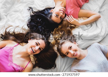 Top view of three  girls   in bed . Group of pretty young women in pajamas lie on back and talk. Sunny warm colors. Cozy atmosphere.