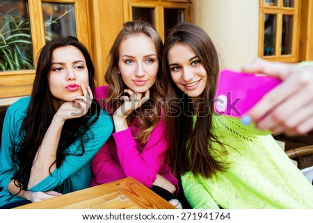 Drinks, friendship, technology and people concept -  Three happy  pretty  women  with cups sitting at table and taking selfie with smartphone in cafe. Bright sunny colors.