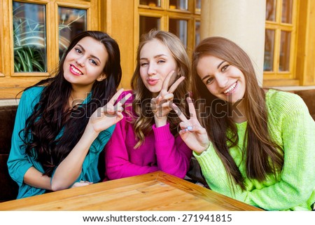 Three stylish pretty girls sitting in cafe   and hugging .  Group of friend enjoying  their time out.