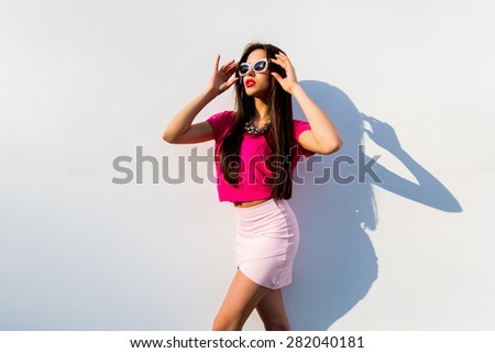 Fashion portrait of glamour bright sexy woman in pink top and skirt with perfect long legs walking against modern urban white   wall  background.