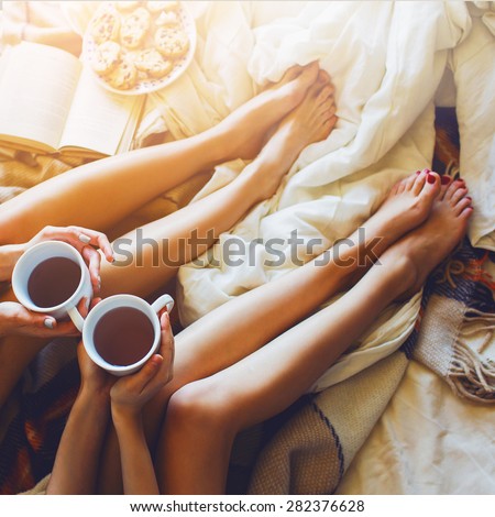 Soft photo of two sisters  in   bedroom with old books and cup of tea in hands wearing cozy sweater , top view point. Two best friends enjoying morning.