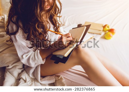 Close up lifestyle  soft  image of  pretty young woman sitting  on her cozy bed  and making notes to her diary.  Fall season mood. Bright colors.