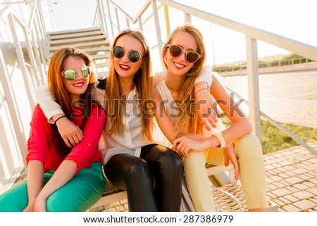 Three best friends  sitting on stairs  and hugging. Group of pretty women in stylish  casual clothes posing  on the street urban background .