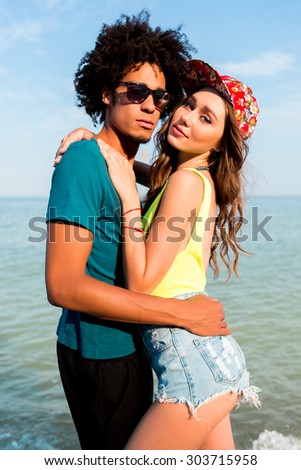 Fashion portrait of stylish  couple  posing on amazing tropical beach. Pretty sexy  slim tan woman and her handsome man looking at camera. Wearing  bright neon   swimwear and  hight jeans shorts .