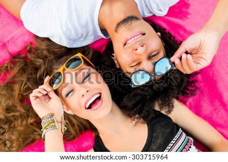 Close up summer portrait of  cheerful young couple  having fun and make grimace. Bright sunny colors .  Beautiful stylish girl and her  handsome man lying on mat. Wearing sunglasses .