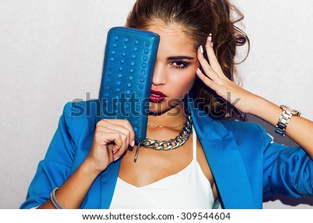Indoor fashion autumn  portrait of elegant  sexy woman in luxury bright glamour outfit, red lips, white crop top and blue jacket. Model holding  hand clutch .