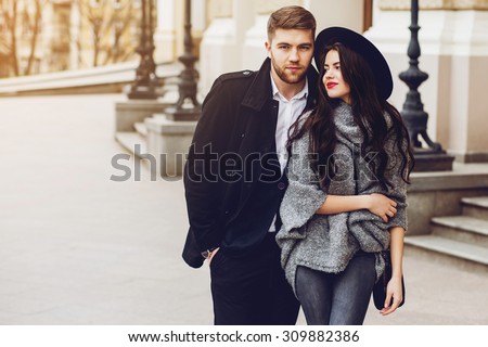 Outdoor fall portrait of fashionable pretty young couple wearing trendy  outfit . Two lovers posing against theater background in autumn sunlight.