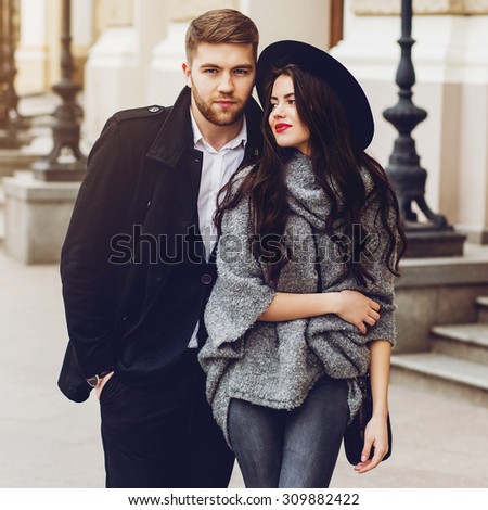 Outdoor fall portrait of fashionable pretty young couple wearing trendy monochrome outfit . Two lovers posing against theater background in autumn sunlight.