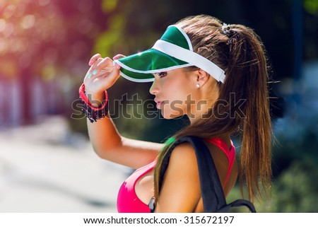 Close up lifestyle portrait  of fitness  pretty young woman  in stylish  cap wearing  pink sports bra  and bright neon backpack. Fresh healthy stylish sport  girl   posing near pool in hot summer day.