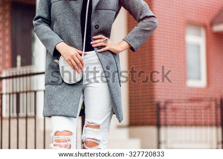 Fashion outdoor portrait of pretty young blonde woman in fall casual outfit grey coat , white trendy torn jeans. Attractive lady walking on the street .Warm colors. Handbag.