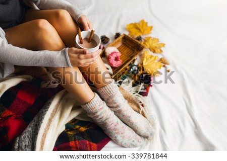 Soft autumn portrait of pretty woman sitting in her bed with books and drinking coffee with cinnamon, cookies and glazed donuts. Top view. Girl in warm knitted handmade clothes at home. Winter season