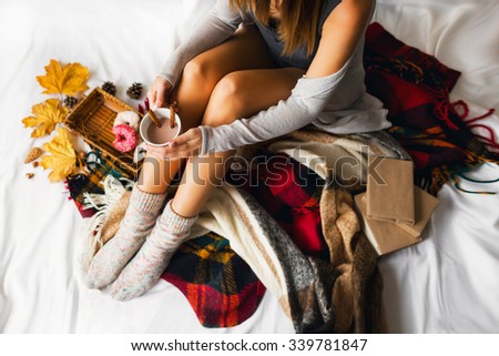 Soft autumn portrait of pretty woman sitting in her bed with books and drinking coffee with cinnamon, cookies and glazed donuts. Top view. Girl in warm knitted handmade clothes at home. Winter season