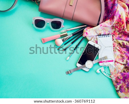 Fashionable female accessories watch sunglasses lipstick  pink  clutch and mobile phone. Overhead of essentials for stylish young woman. Different objects on blue  background . Bright summer colors.