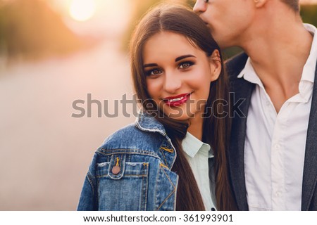 Close up lifestyle  toned image of young couple in love hugging. . Pretty young girl in jeans  jacket  looking at camera  and her handsome boyfriend   kissing her . Romantic mood.