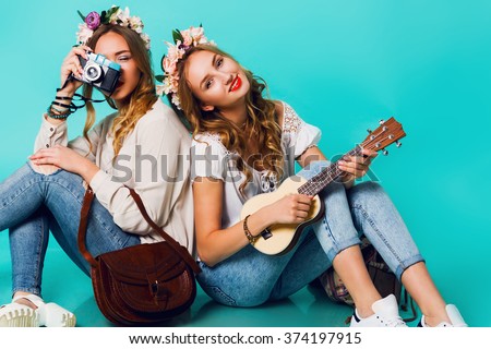 Studio lifestyle portrait of two pretty young blonde happy girls having fun. Making pictures in hipster style on retro camera, wearing stylish vintage boho outfits and flowers wreath. Spring.