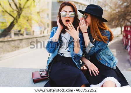 Two  pretty cuter teenagers  shares secrets, gossip. Surprise face, emotions,  Best friends wearing stylish outfit, black hat, sunglasses, dress. Bright spring  colors.