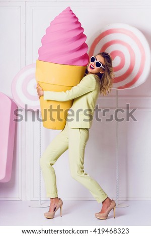 Cute fashionable woman  holding big props pink  ice cream, walking on hight heels  and laughing. Wearing bright elegant costume , stylish vintage  sunglasses.