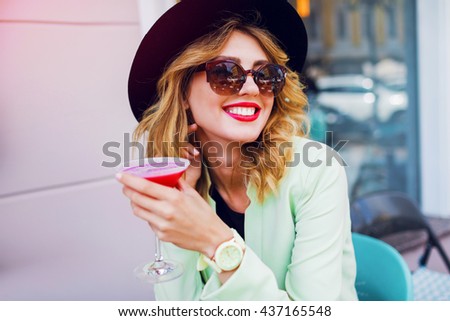 Stylish pretty woman in casual  outfit, black hat and neon jacket drinking sweet tasty beverage. Enjoying her holidays and relax. Bright summer colors. Positive mood.