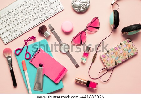 Top view of stylish  ladies lifestyle accessories. Pastel Colors Trend. Pink notebook, trendy  hearts sunglasses,turquoise headphones,brushes,lipstick,nail polish,keyboard on pink tender background.