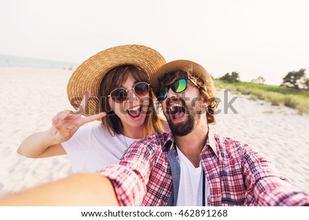 Happy  traveling  couple in love  taking a selfie on phone  at the beach on a sunny summer day.  Pretty girl and her handsome boyfriend with beard    having fun, crazy emotional faces , laughing.