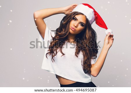 Young sexy new year woman with long brunette hair and pretty face , bright make up  in red christmas santa claus holiday  hat posing  on white background  with snowflakes. Emotion surprised face.