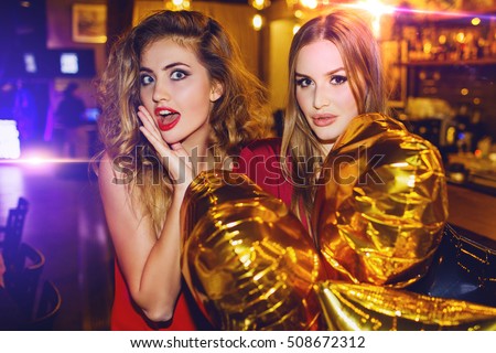 Two girls, happy stylish friends  celebrating new year or birthday  party holding gold stars balloons, surprised faces.  Fashion  elegance  women enjoying time together.