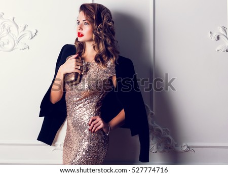 Close up portrait of elegant luxurious woman in trendy gold sequin party dress . Elegant wavy hairstyle, bright make up, red lips. Holding trendy evening purse.