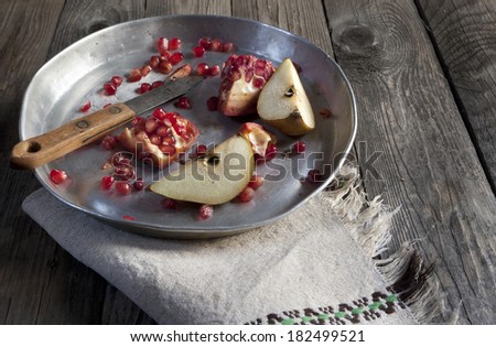 fruits composition with pomegranate grains and pear on silver vintage tray and napkin on wooden table