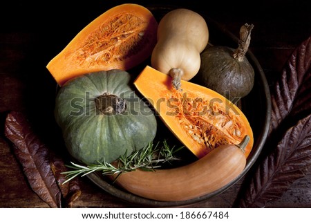 still life with whole fruits and vegetables like banana, lemon, apple, pear, red pepper, garlic on basket with wooden chopping board and ceramic pot in rustic background