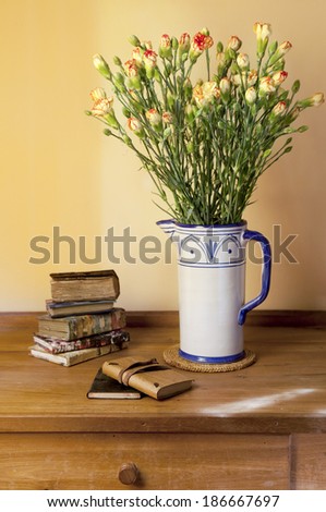 carnation flowers bouquet in ceramic vase on wooden rustic table with books and little agendas