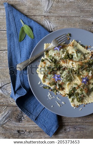 italian handmade pasta ravioli with borage herb, flower, sage, crisp onion on plate on rustic wooden table