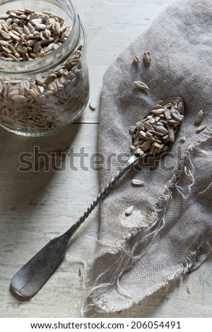 Silver spoon with sunflower seeds on jute on wooden white background