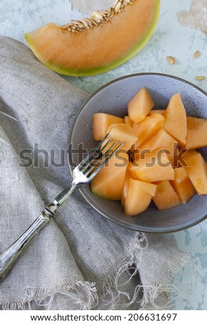 fresh pieces of melon on bowl and slices on vintage scraped blue background with jute napkin and fork