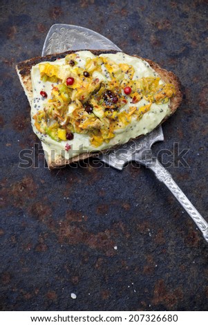 toasted bread snack with basil sauce and zucchini blossoms on rust scraped background with vintage silver scoop